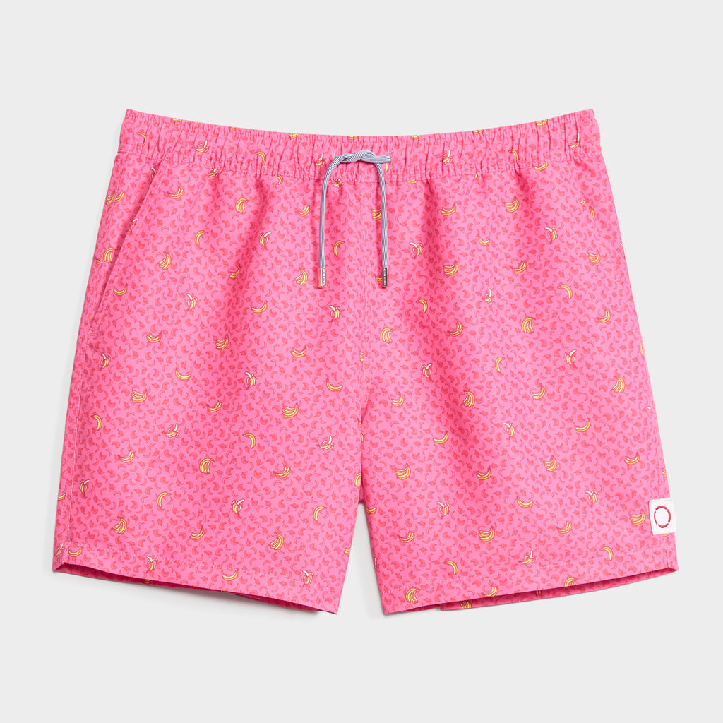 PEEL PARTY swim trunks by PUBLIC BEACH SWIM feature a bright pink banana print with small yellow bananas, a grey drawstring waist, and a white patch with red circle on the lower right leg. Quick-dry fabric stands out against the light grey backdrop.