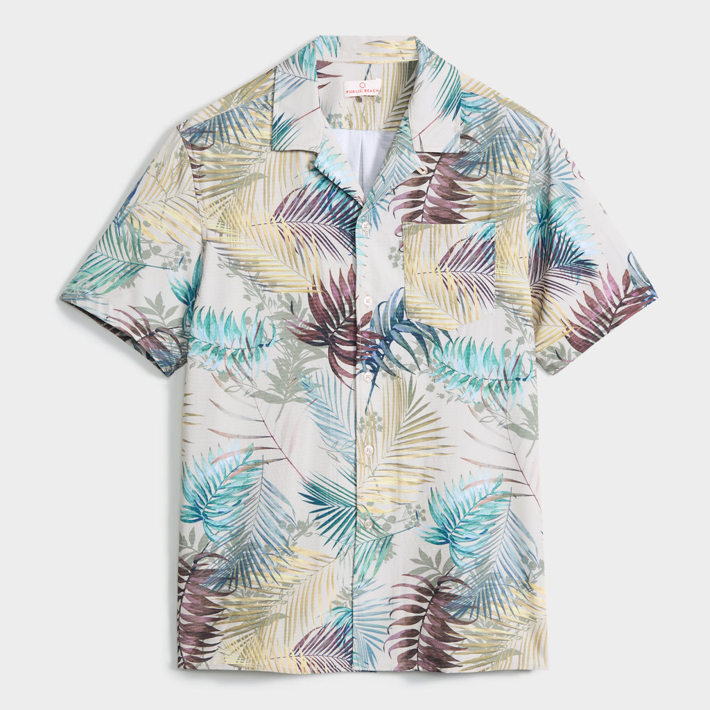 The BOTANIC BURST SHIRT by PUBLIC BEACH SWIM is a men’s button-up with a single chest pocket, showcasing a botanical palm print in blue, green, beige, and burgundy on a light background—ideal for cool summer style.