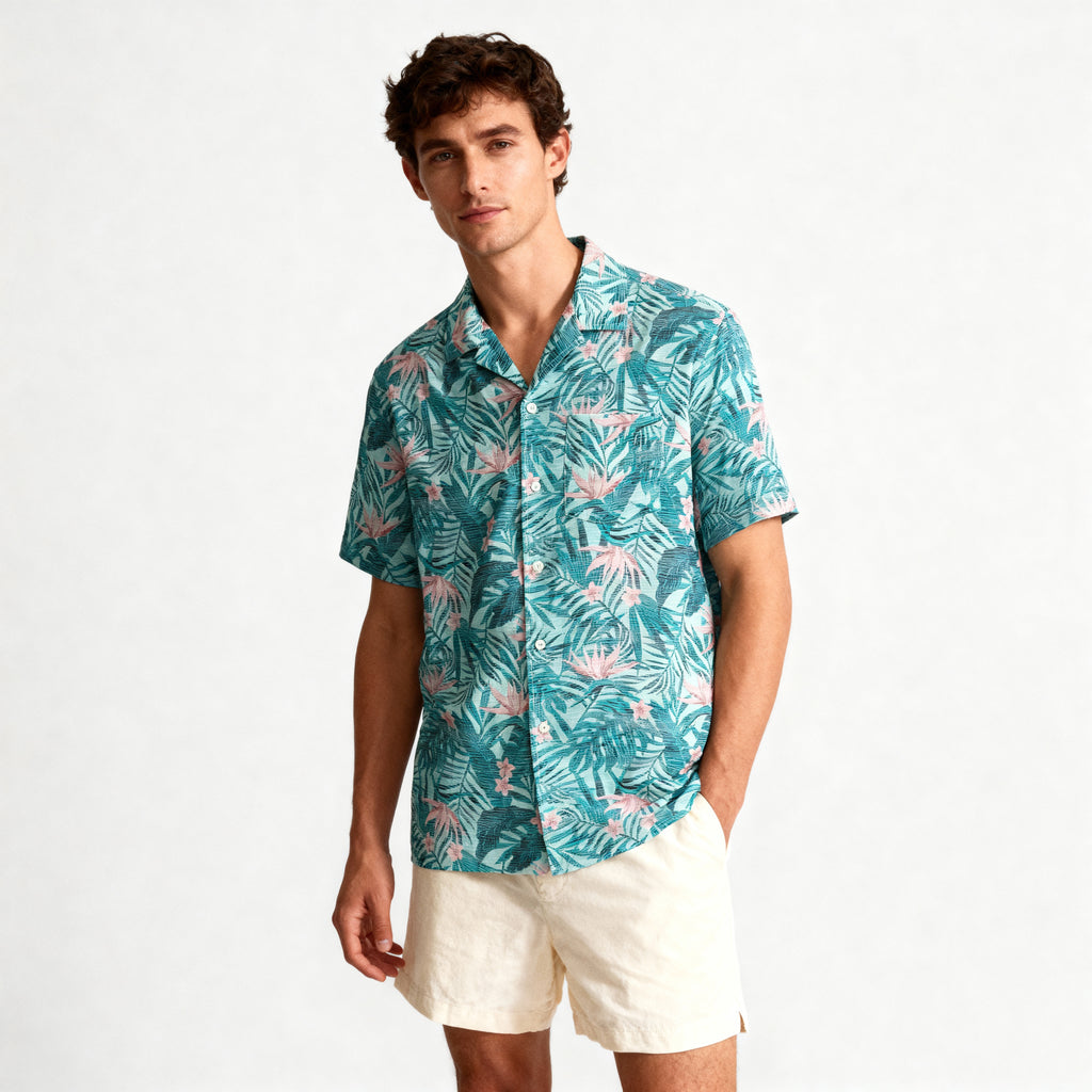 A man in a teal TROPICAL PULSE SHIRT by PUBLIC BEACH SWIM, made from seersucker fabric, and light beige shorts stands against a white background, looking at the camera with a neutral expression.