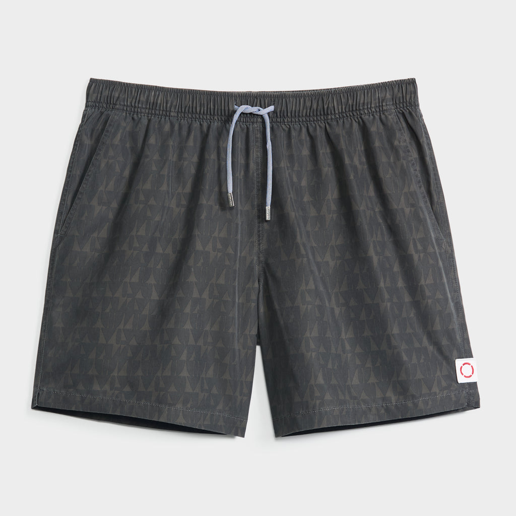 The PRISM FLOW men’s swim shorts by PUBLIC BEACH SWIM feature a dark gray geometric triangle print, an elastic waistband with a light gray drawstring, and a small white patch with red circle on the lower left leg.