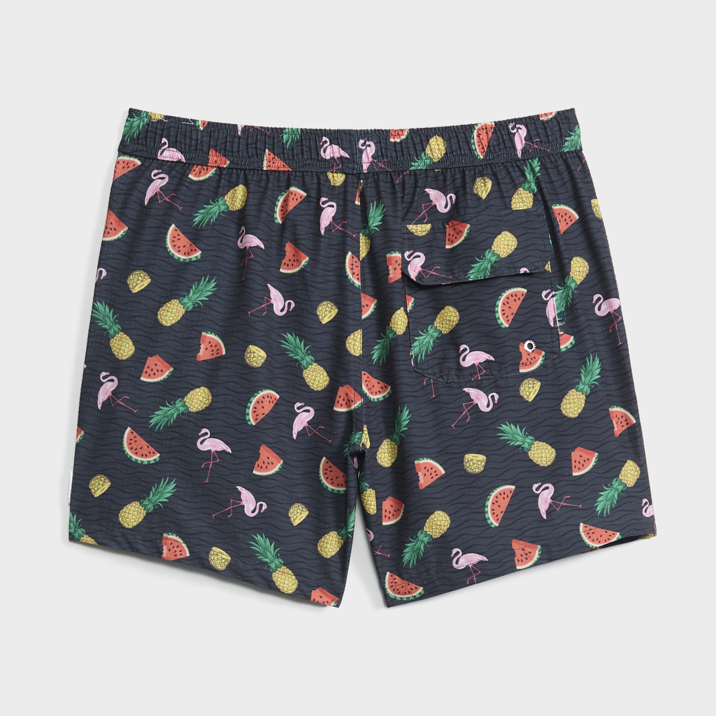 The TROPICAL TANGO swim shorts by PUBLIC BEACH SWIM feature a dark tropical print with pink flamingos, pineapples, and watermelon slices, plus a right-side back pocket with a logo patch.