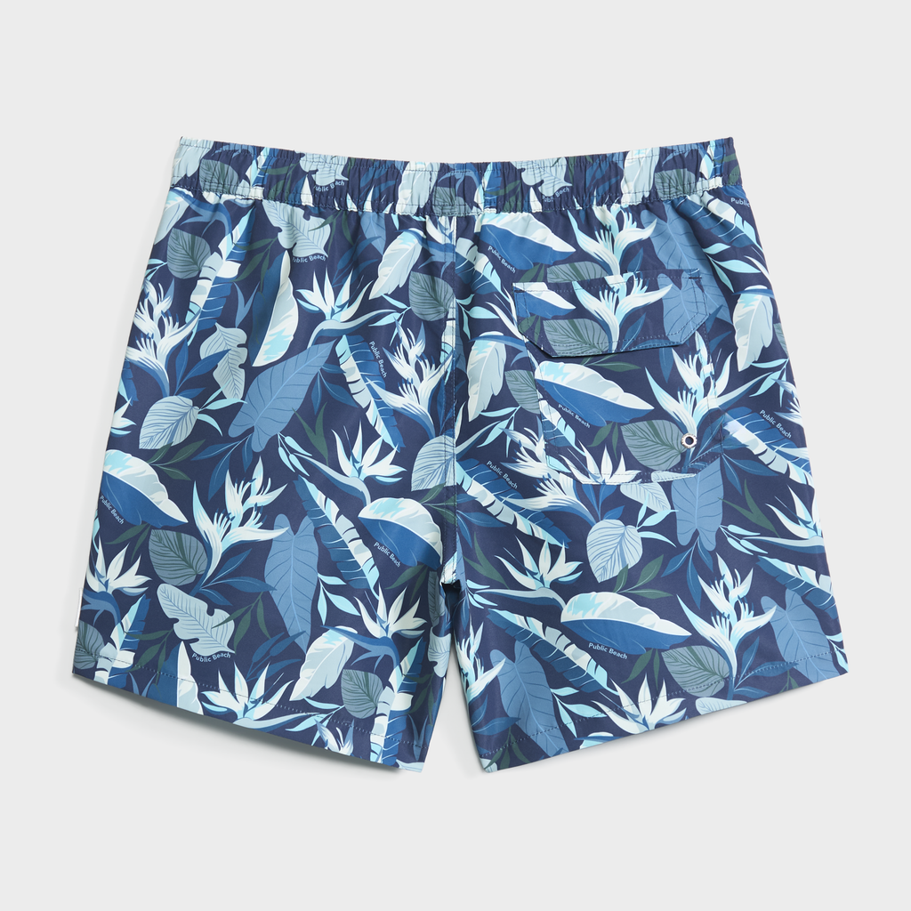 The BLOOMING TROPIC swim trunk by PUBLIC BEACH SWIM features an elastic waistband, quick-dry blue and white floral print, and a back pocket with drainage—a stylish choice for sunny days.