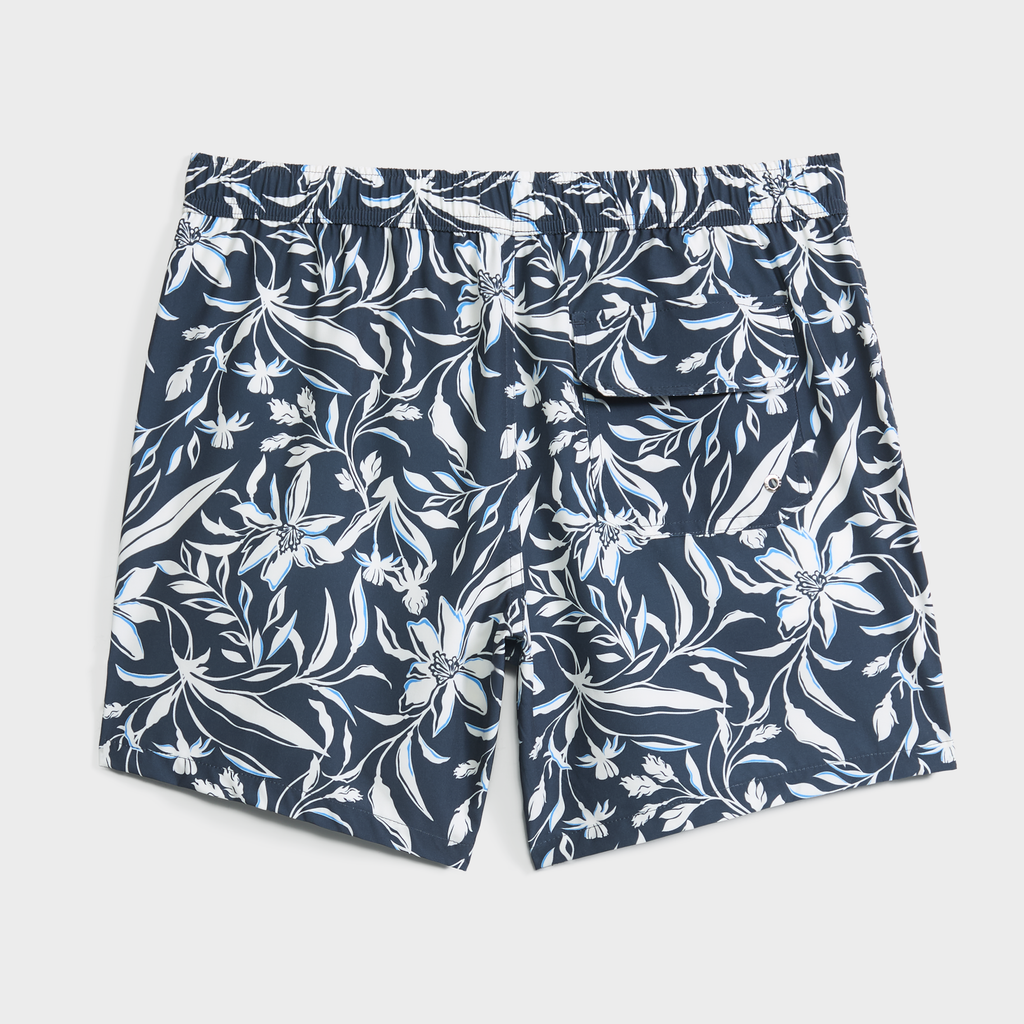 PUBLIC BEACH SWIM's FLORAL IVY swim trunks feature a navy blue and white tropical floral pattern, elastic waistband, and back flap pocket. Quick-dry essentials are shown laid flat on a plain white background.