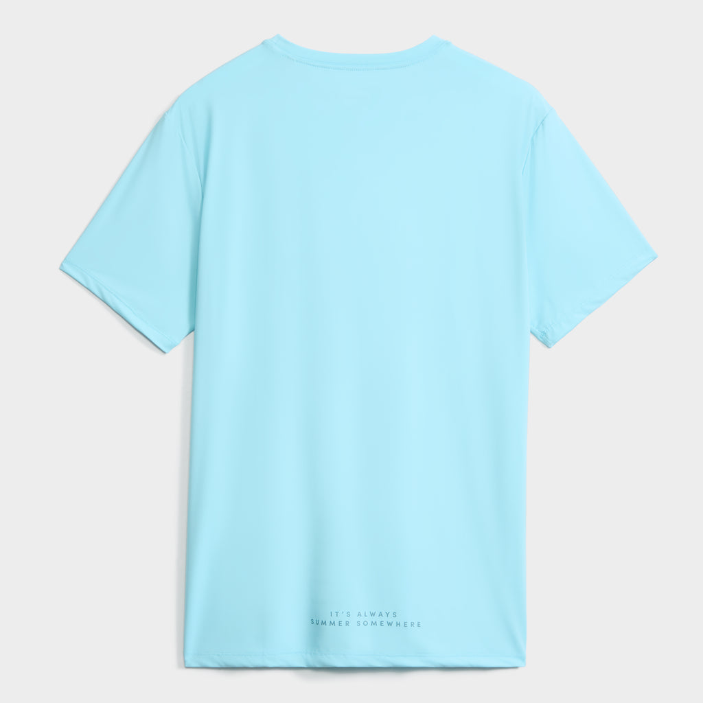 The PUBLIC BEACH SWIM SHORT SLEEVE RASHGUARD for men is shown from the back in light blue, with "ITS ALWAYS SUMMER SOMEWHERE" near the hem. This quick-drying shirt offers UPF 50 sun protection for all-day comfort.