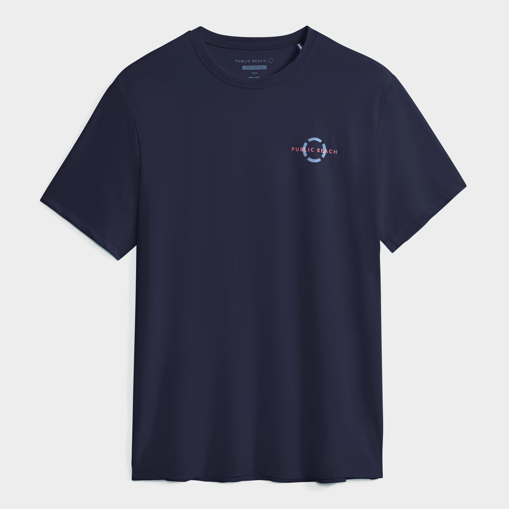 The PUBLIC BEACH SWIM SHORT SLEEVE RASHGUARD features a navy blue design, left chest circular "PUBLIC BEACH" graphic, and UPF 50 sun protection. Perfect for safety and style. Shown on a plain white background.
