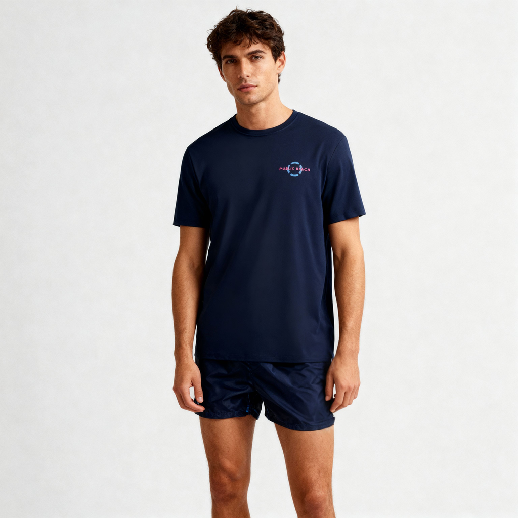 A young man with short brown hair wears the PUBLIC BEACH SWIM SHORT SLEEVE RASHGUARD and matching shorts, standing against a plain light background—perfect for stylish UPF 50 sun protection.
