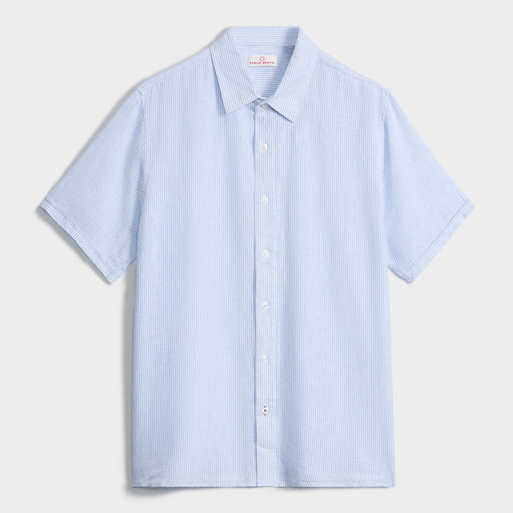A light blue PUBLIC BEACH SWIM STRIPE SHIRT with a subtle striped pattern, white buttons, and a classic collar is laid flat on a white background.