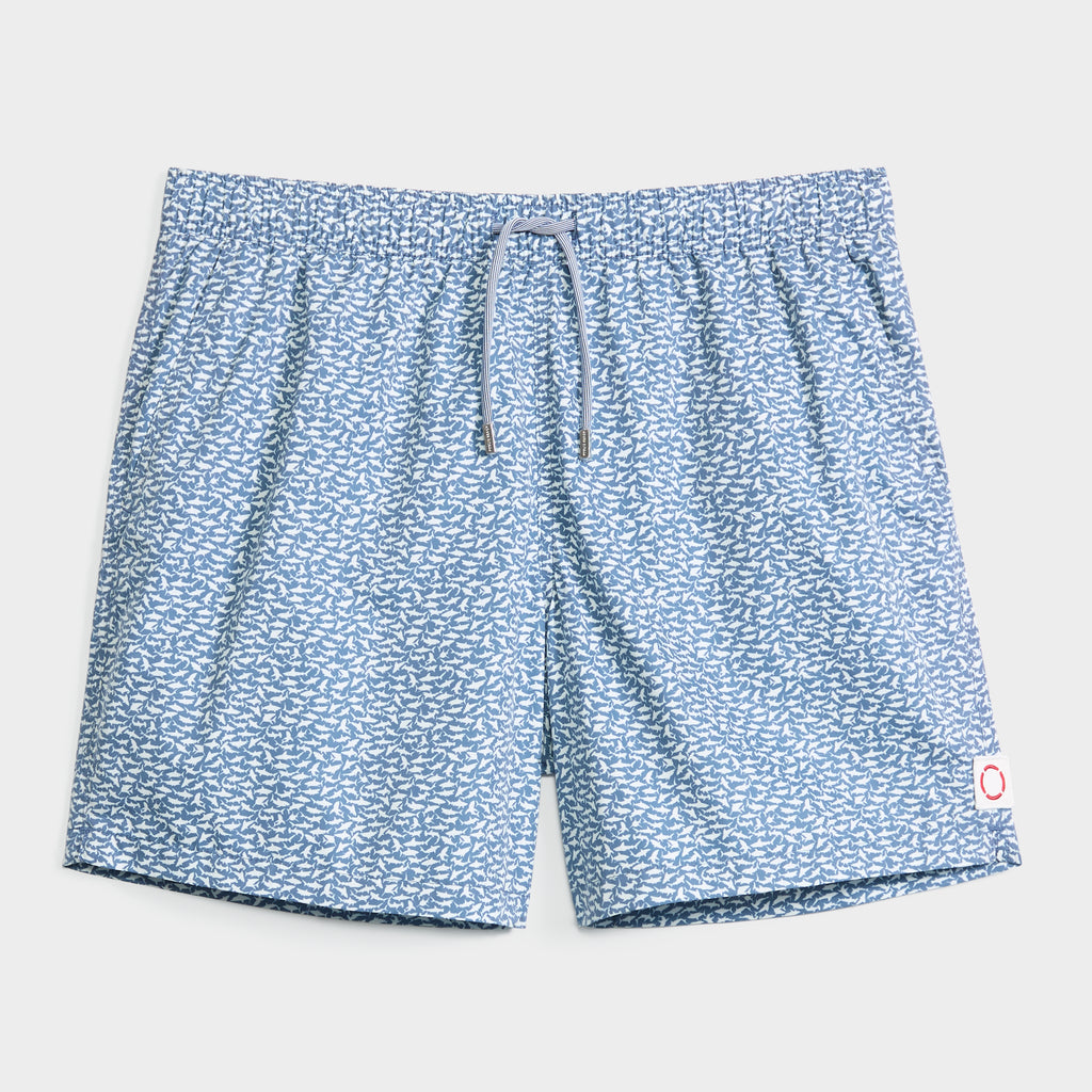 The PUBLIC BEACH SWIM JAWSOME swim short comes in light blue with a white fish pattern, quick-dry fabric, elastic waistband, gray drawstring, and a white patch with a red circle on the bottom right hem.