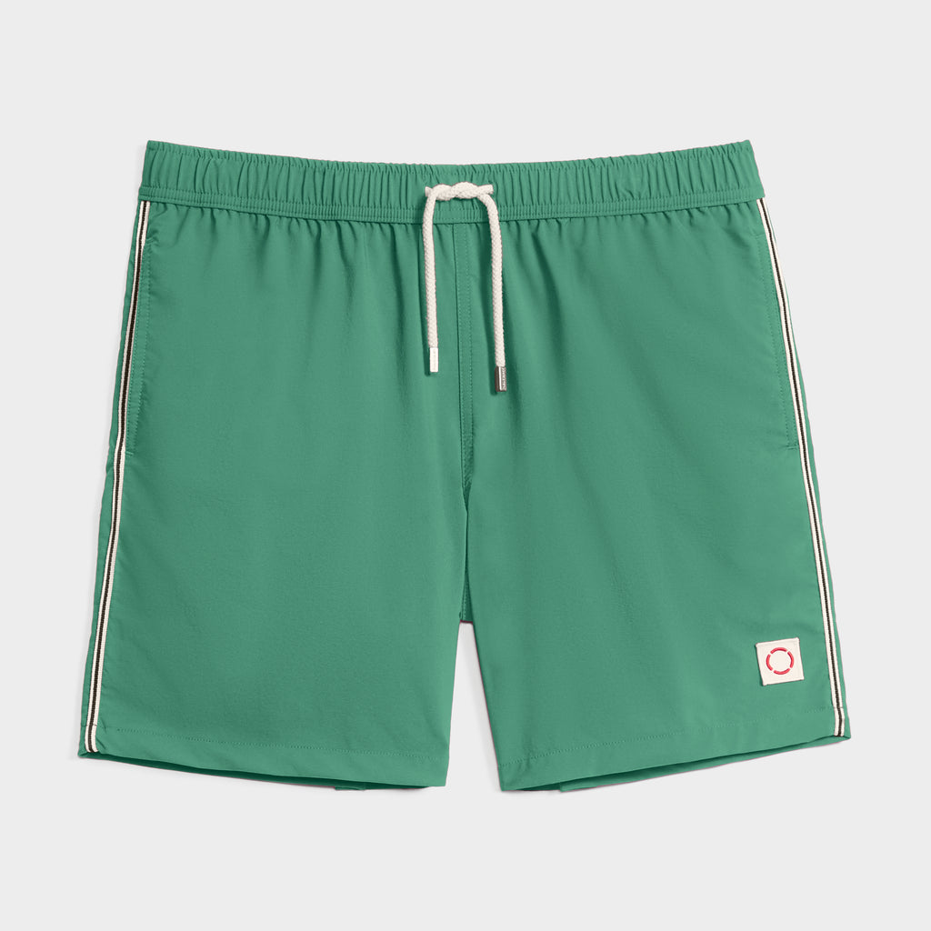 THE VINTAGE swim shorts by PUBLIC BEACH SWIM feature a green design with a white drawstring, side stripes, and a small white patch with a red circle—retro-inspired beachwear laid flat on a light background.