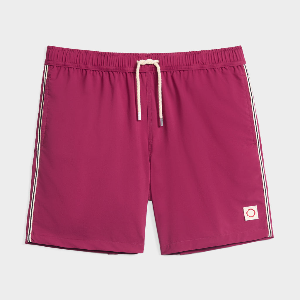 THE VINTAGE men's swim shorts by PUBLIC BEACH SWIM in magenta with white side stripes, elastic waistband, white drawstring, and a small square red-circle patch near the left hem—classic beachwear style laid flat on white.