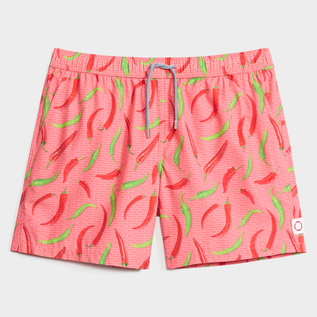 PUBLIC BEACH SWIM's HOT PEPPERS men's swim shorts feature a vibrant chili pepper print on pink, quick-dry fabric, an elastic waistband with gray drawstring, and a small white patch on the lower right leg.