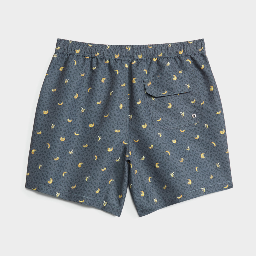 The PEEL PARTY swim shorts by PUBLIC BEACH SWIM feature a dark gray base with an all-over yellow banana print, elastic waistband, buttoned back pocket with drainage grommet, and are made from quick-dry fabric. Shorts shown laid flat on white background.